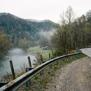 Two-lane river road following a wide West Virginia river with early spring hillsides above