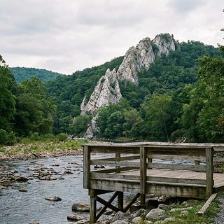 A tall gray quartzite fin standing above a green valley with a shallow river running past pastureland below